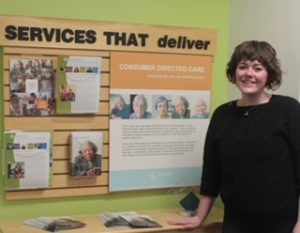 Care Advisor standing next to bulletin board that says "Services that deliver"