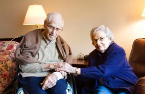 elderly Caucasian man and woman sitting holding hands