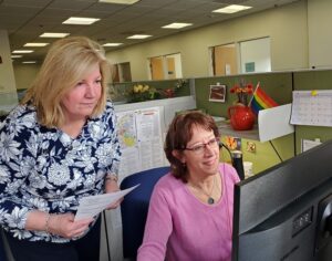 women standing behind another woman working together in office cubicle